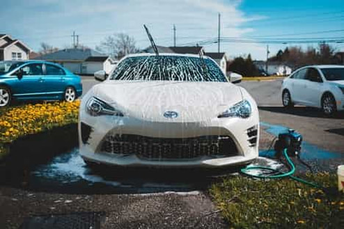Picture of a white car being hose washed with a water compressor machine